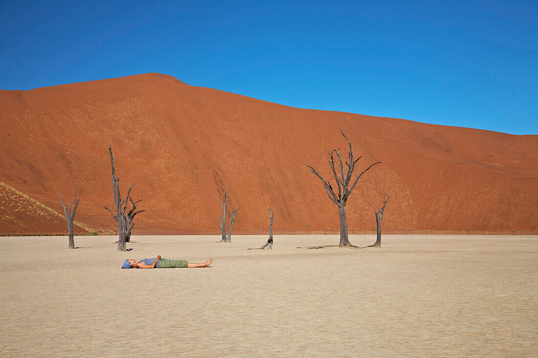 Frau liegt auf dem Boden, Salzsee mit toten Bäumen, Namib Naukluft Park, Sossusvlei, Namibia, Afrika