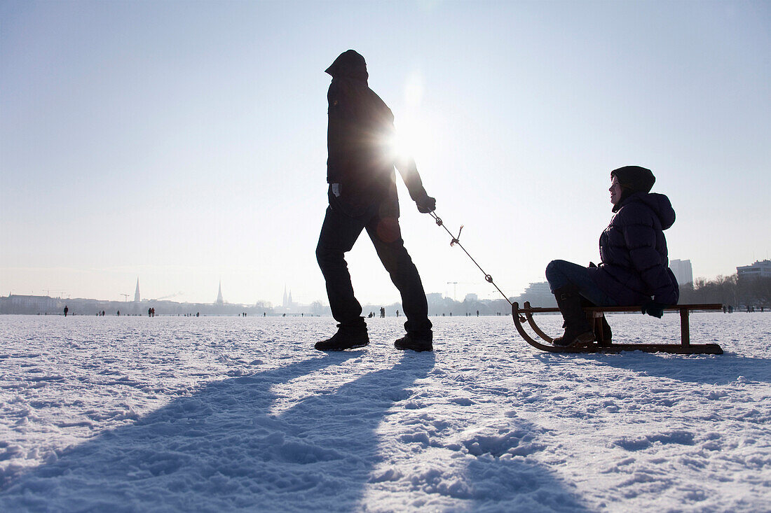 Zwei Personen mit einem Schlitten auf zugefrorener Außenalster im Winter, Hamburg, Deutschland