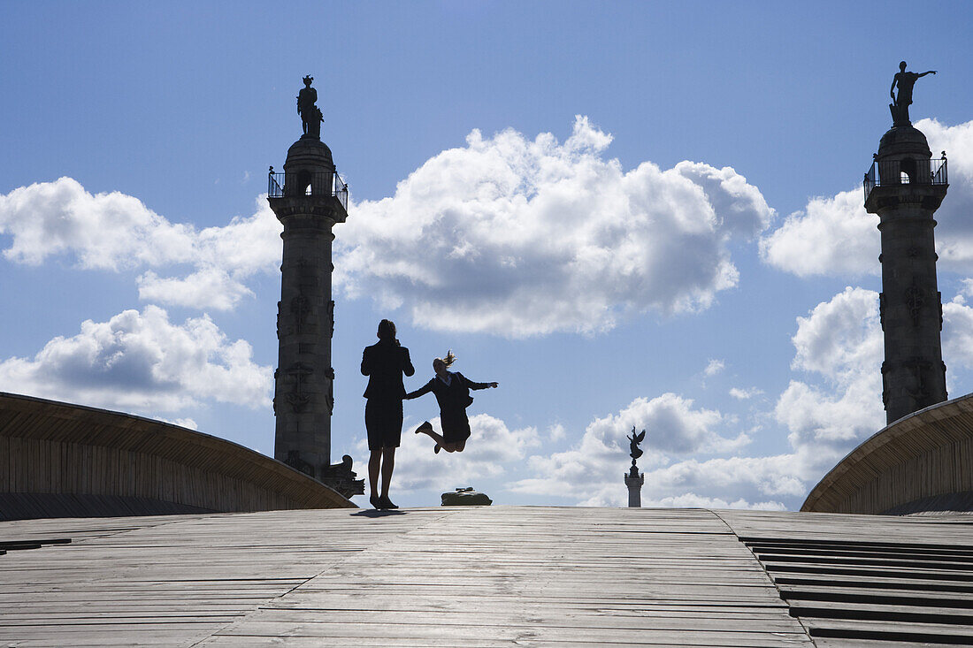 Mädchen springen auf Holzbrücke mit Statuen im Hintergrund, Bordeaux, Gironde, Aquitanien, Frankreich, Europa