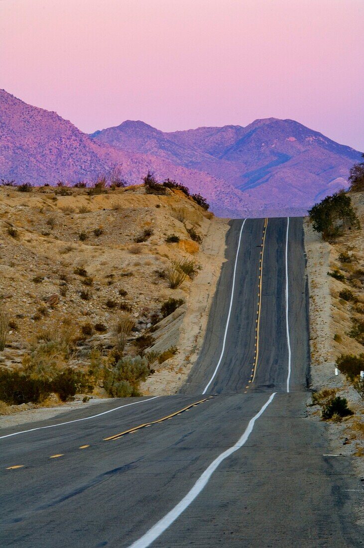 Sunrise on mountains over two lane desert road on a hill, Anza Borrego Desert State Park, San Diego County, California