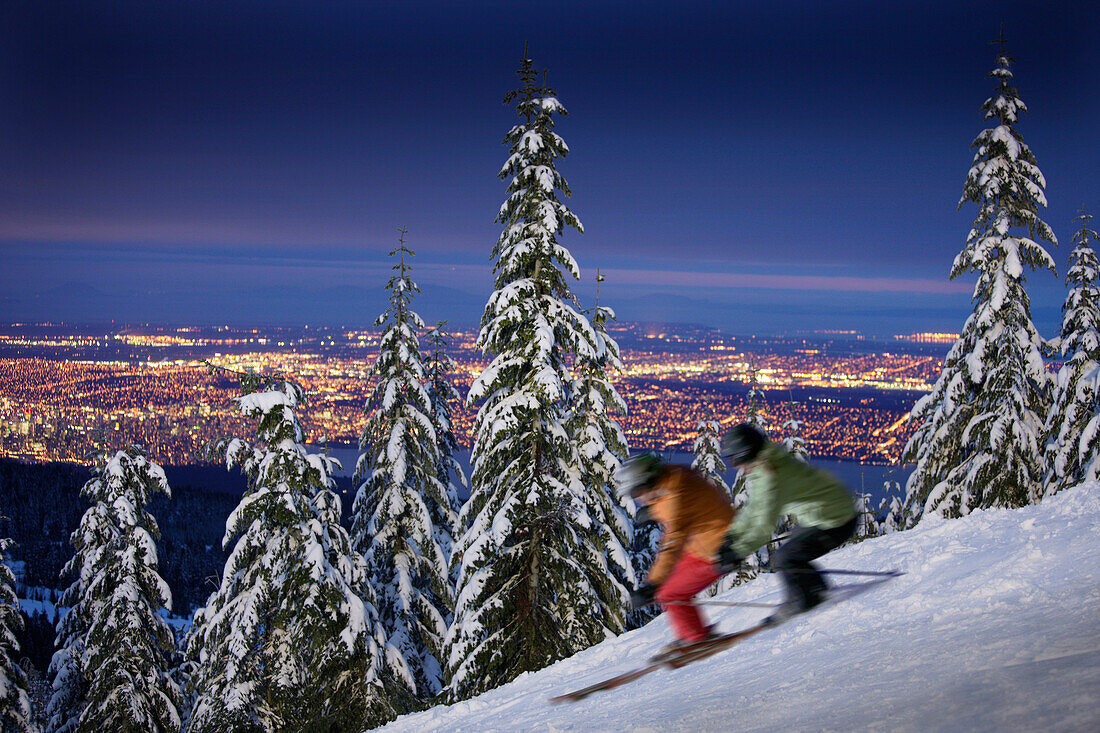 Skiers on slope in floodlight, Vancover in background, British Columbia, Canada