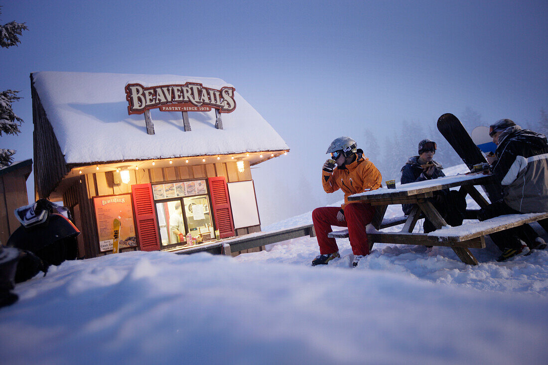 Skiers and snowboarders resting beside snack stall, Grouse Mountain, British Columbia, Canada