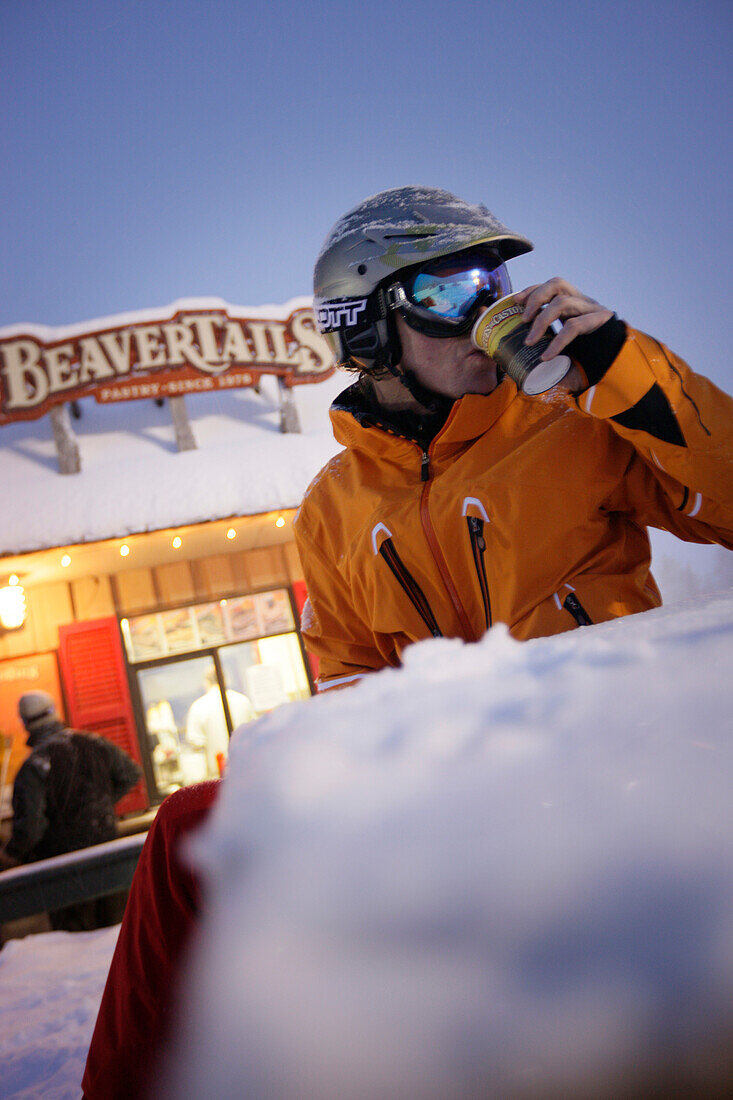 Skier having a cup of coffee, snack stall in background, Grouse Mountain, British Columbia, Canada