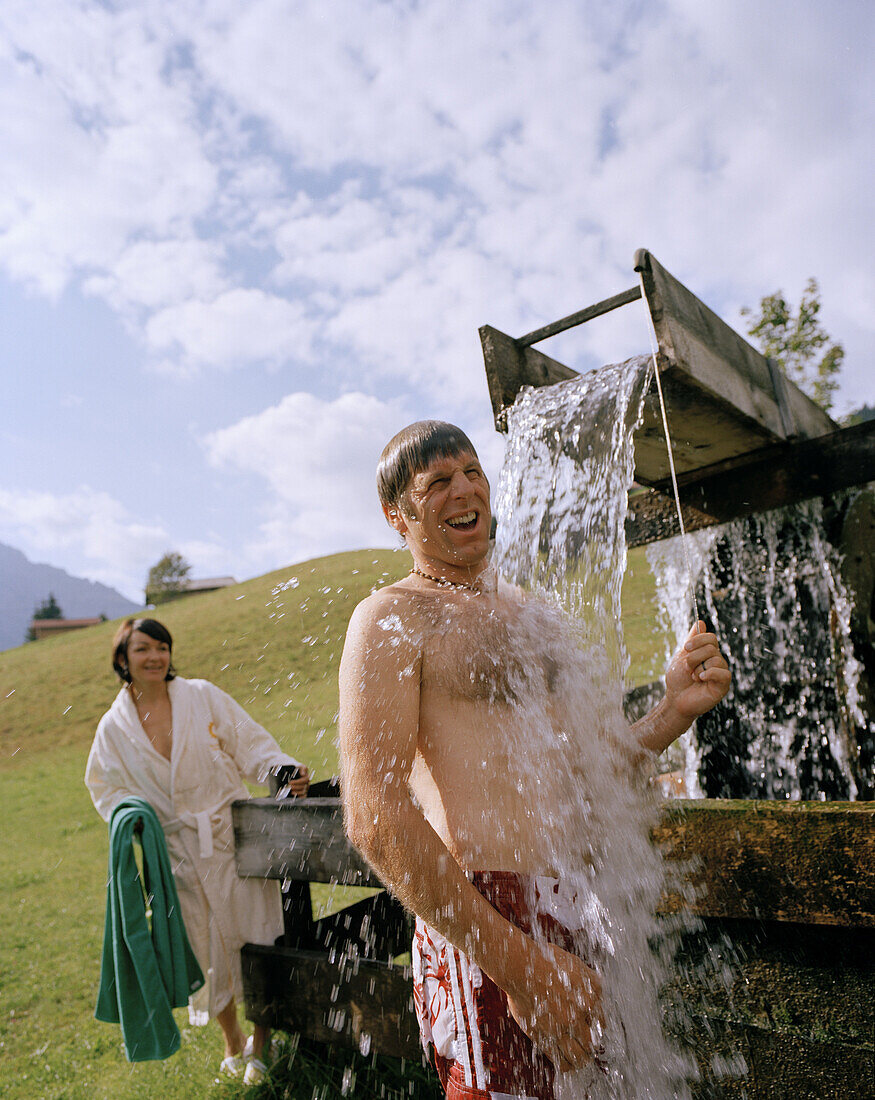 Mann nimmt eine erfrischende, kalte Dusche, Aussendusche, Naturhotel Chesa Valisa, Hirschegg, Kleinwalsertal, Österreich