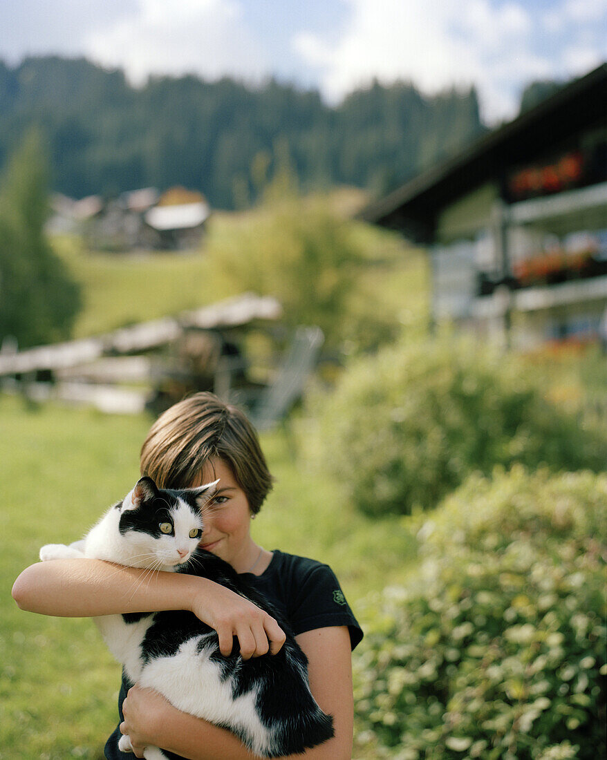Young girl hugging cat outside organic Hotel Chesa Valisa, Hirschegg, Kleinwalsertal, Austria