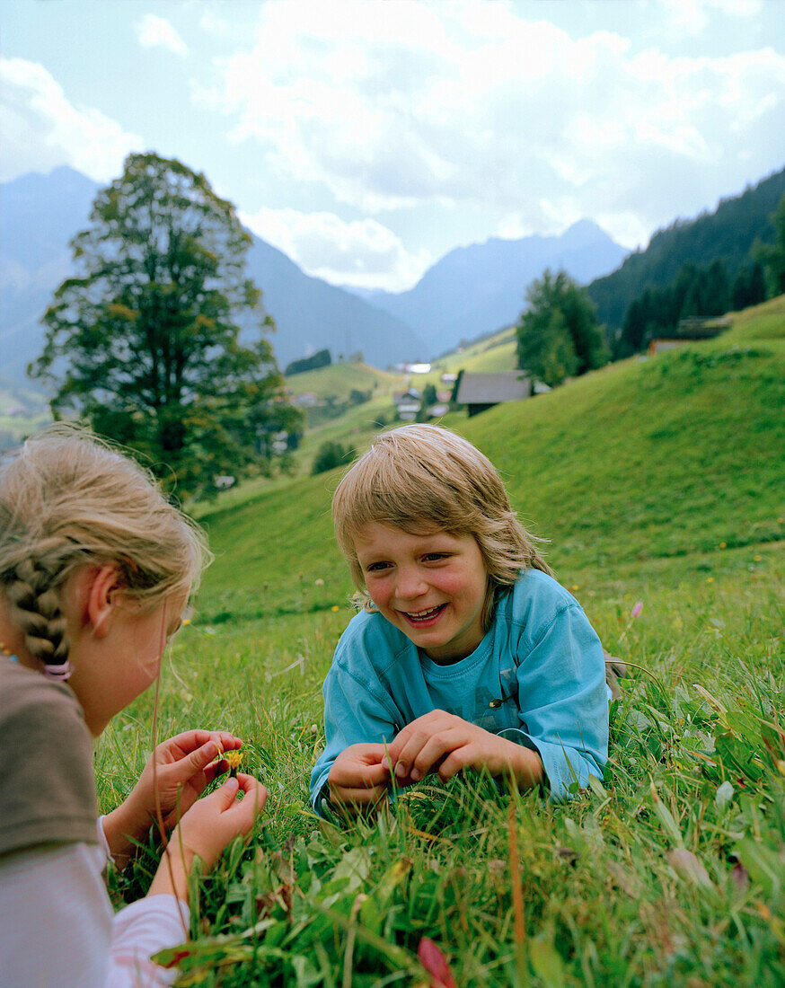 Girl and boy lying in a meadow,  Hirschegg, Kleinwalsertal, Styria, Austria