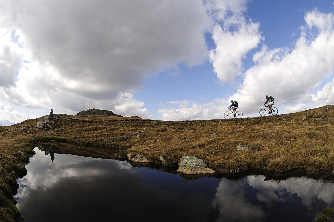 Mountainbiker vor Bergsee unter Wolkenhimmel, Markinkele, Innichen, Hochpustertal, Südtirol, Dolomiten, Italien, Europa