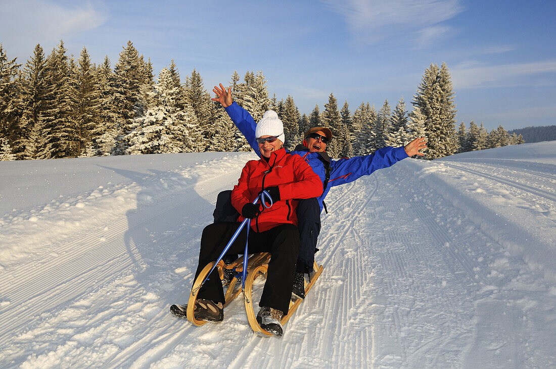 Paar fährt Schlitten auf Winterwanderweg in verschneiter Landschaft, Hemmersuppenalm, Reit im Winkl, Chiemgau, Bayern, Deutschland, Europa