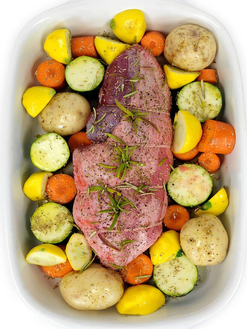 An uncooked lamb roast with vegetables in a baking tray