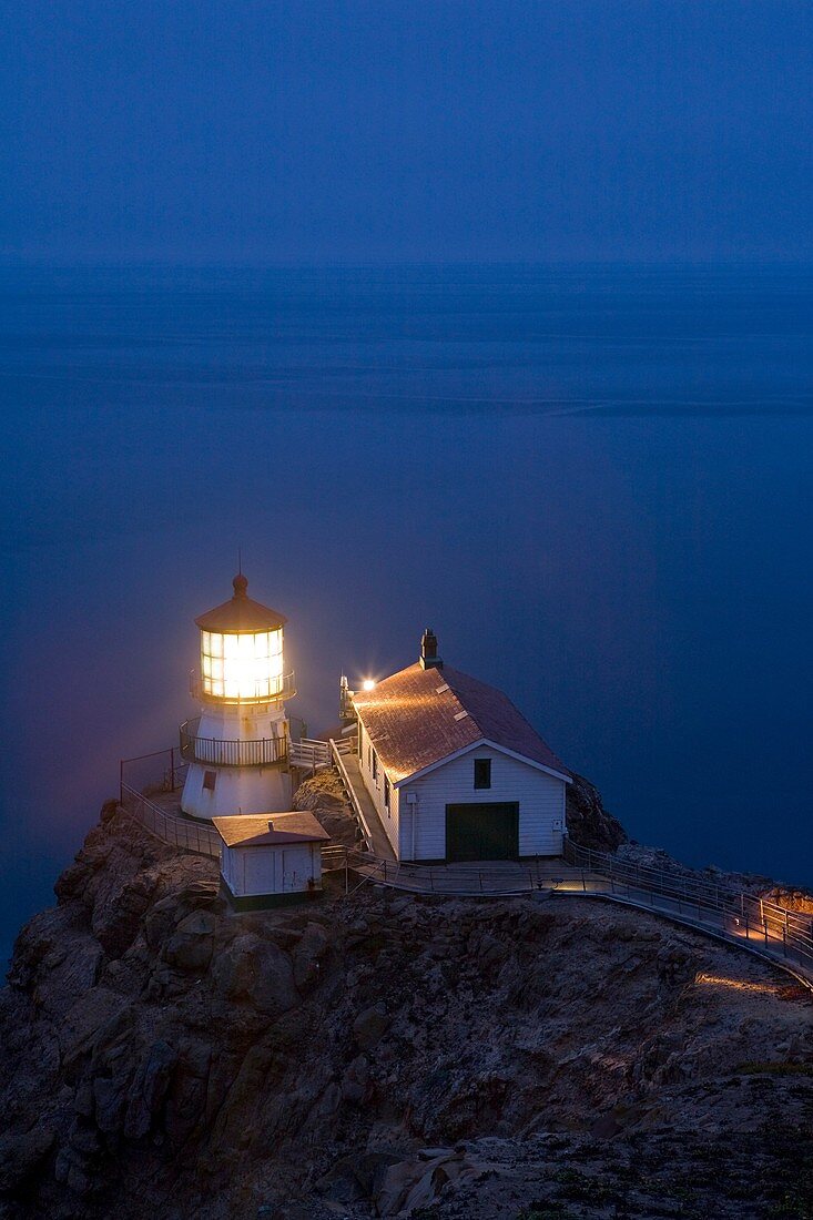 USA, California, Marin County, Point Reyes National Seashore, old lighthouse on the left, modern light on the right, perched on point of Point Reyes Conglomerate rock, staircase for visitors, dusk, vertical