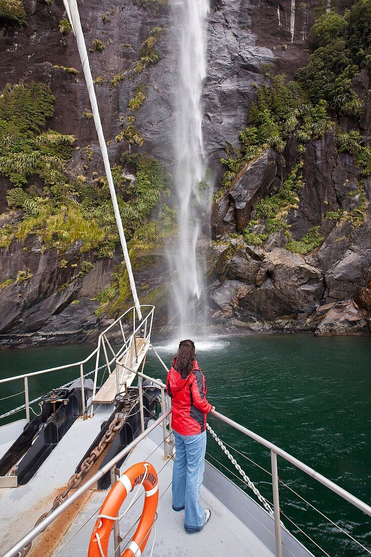 Tourist on bow of Milford Mariner as boat approaches Stirling falls, Milford Sound, Fiordland National Park, New Zealand