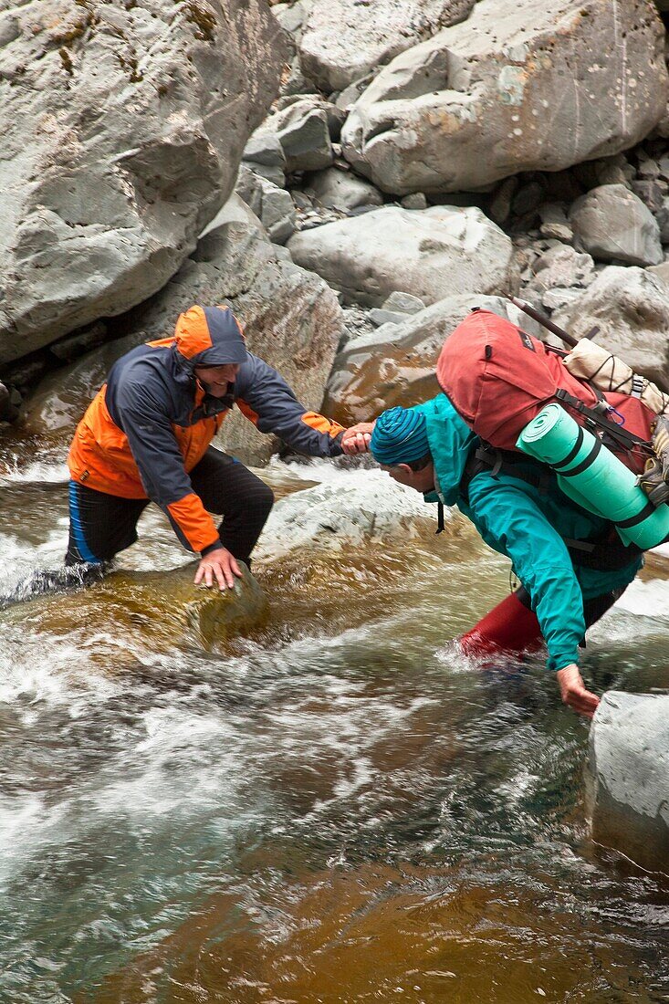 Trampers assisting each other to cross fast flowing Canyon Creek, Canterbury, New Zealand