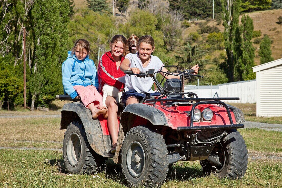 Upcot Station girls with pet spaniel ride quad bike on farm, Upper Awatere valley, Marlborough, New Zealand