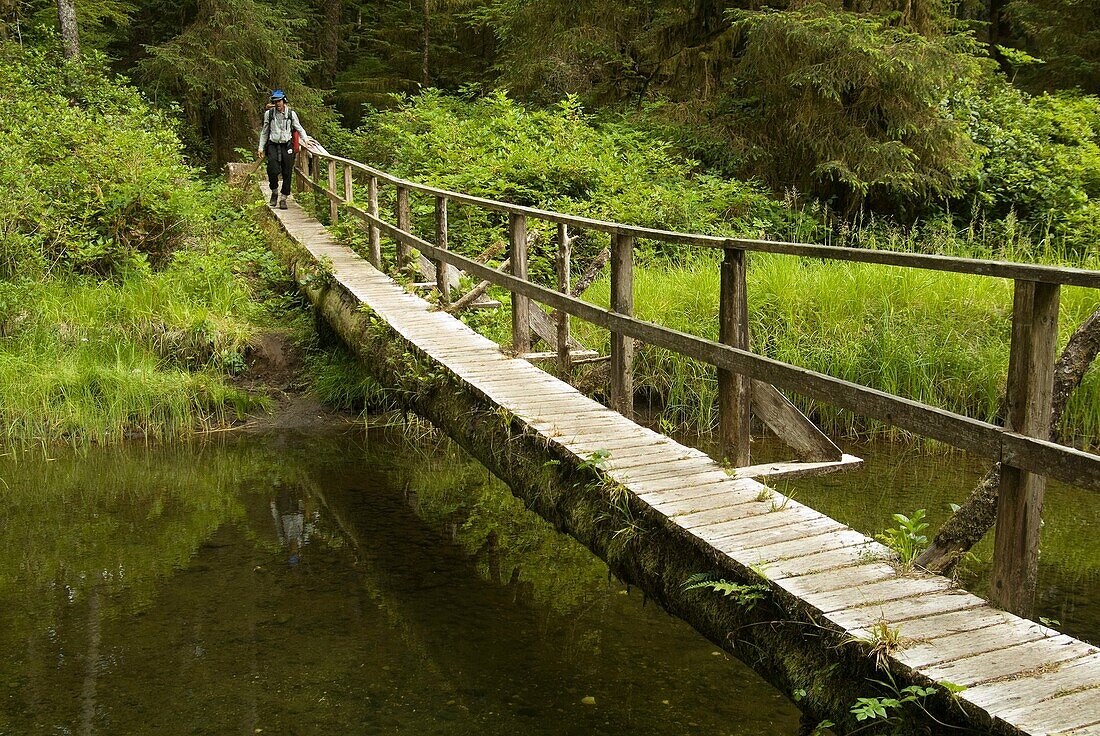A hiker crosses a bride over a stream on Flores Island, Clayoquot Sound, British Columbia, Canada