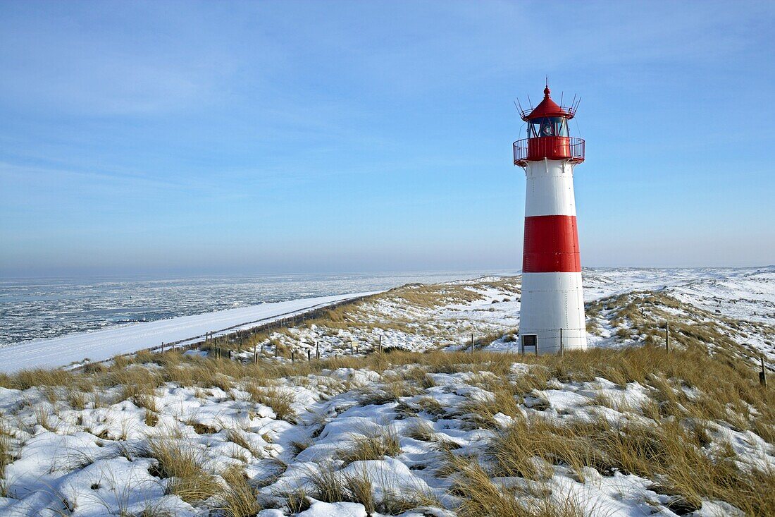 Lighthouse List East on snow covered dunes with a bright blue sky at a sunny day with icy sea in the background, Sylt, Northfrisian Islands, Schleswig-Holstein, Northern Germany, Europe