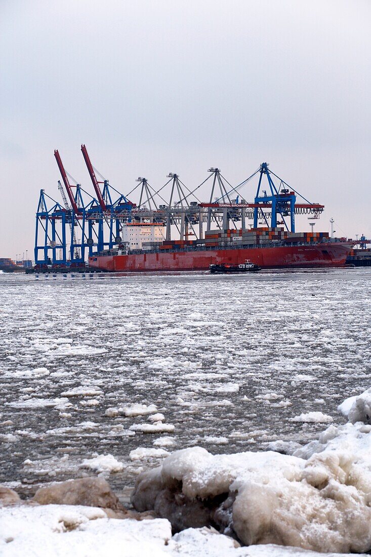 Container ship at a container terminal in the river Elbe filled with ice floes, harbor of Hamburg, Northern Germany, Europe