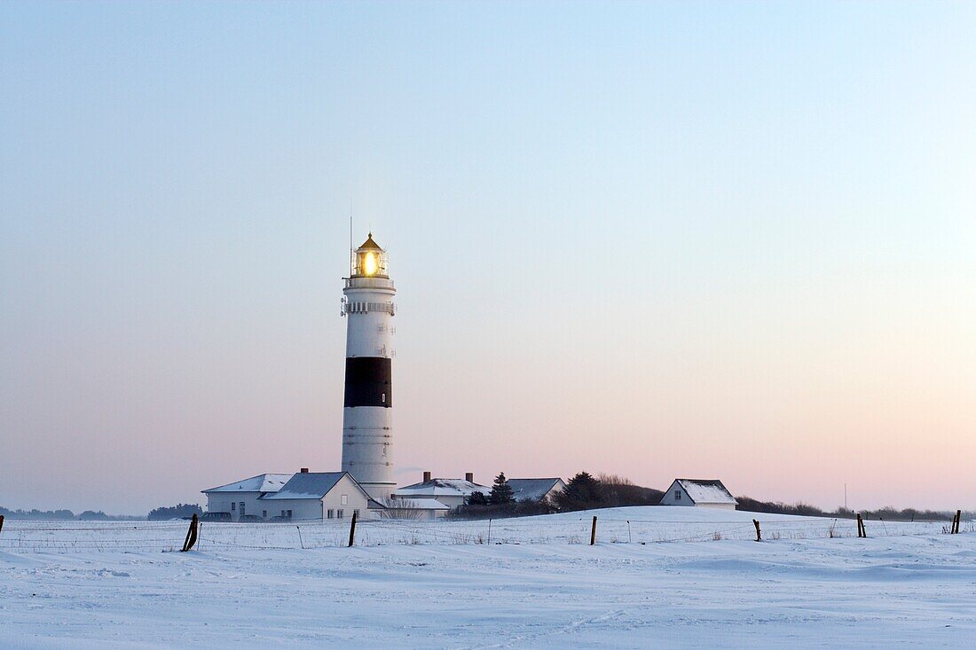 Lighthouse Kampen on snow covered fields with a bright blue sky during sun set, in operation with the light beam visible, Sylt, Northfrisian Islands, Schleswig-Holstein, Northern Germany, Europe