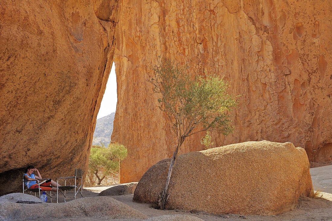 Frau sitzt vor Felswand aus rotem Granit, Spitzkoppe, Namibia