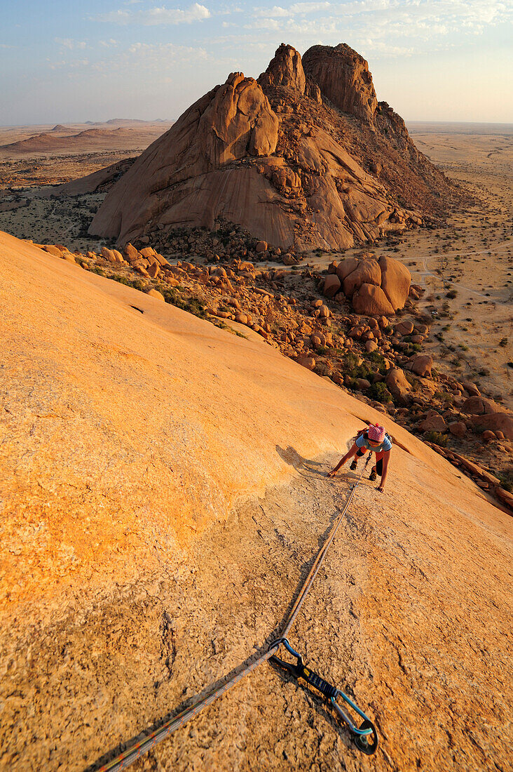 Frau klettert an roter Felswand, Sugarloaf im Hintergrund, Große Spitzkoppe, Namibia