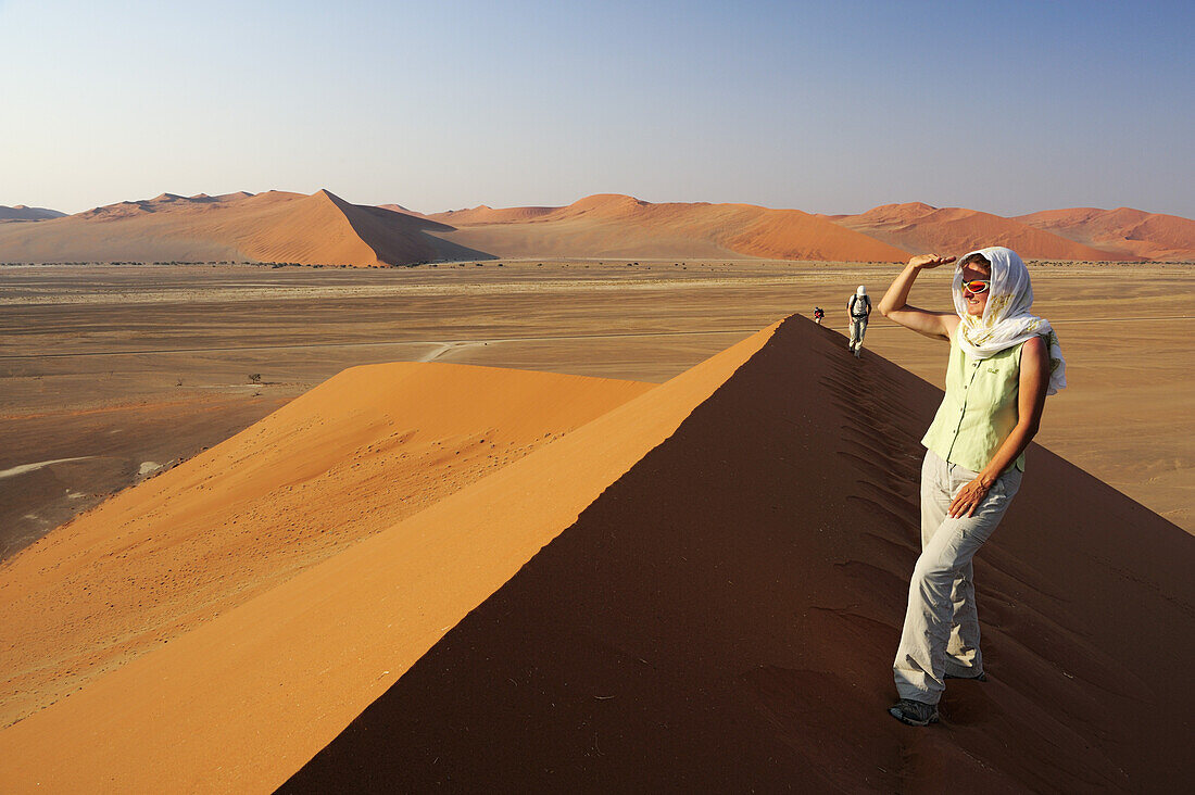 Frau steht auf roter Sanddüne und genießt Aussicht im Sossusvlei, Düne 45, Sossusvlei, Namib Naukluft National Park, Namibwüste, Namib, Namibia