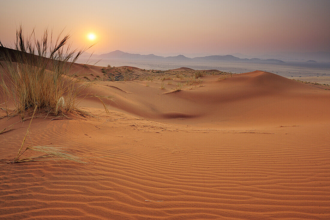 Sonnenaufgang über roten Sanddünen mit Tirasberge im Hintergrund, Namib Rand Nature Reserve, Namibwüste, Namibia