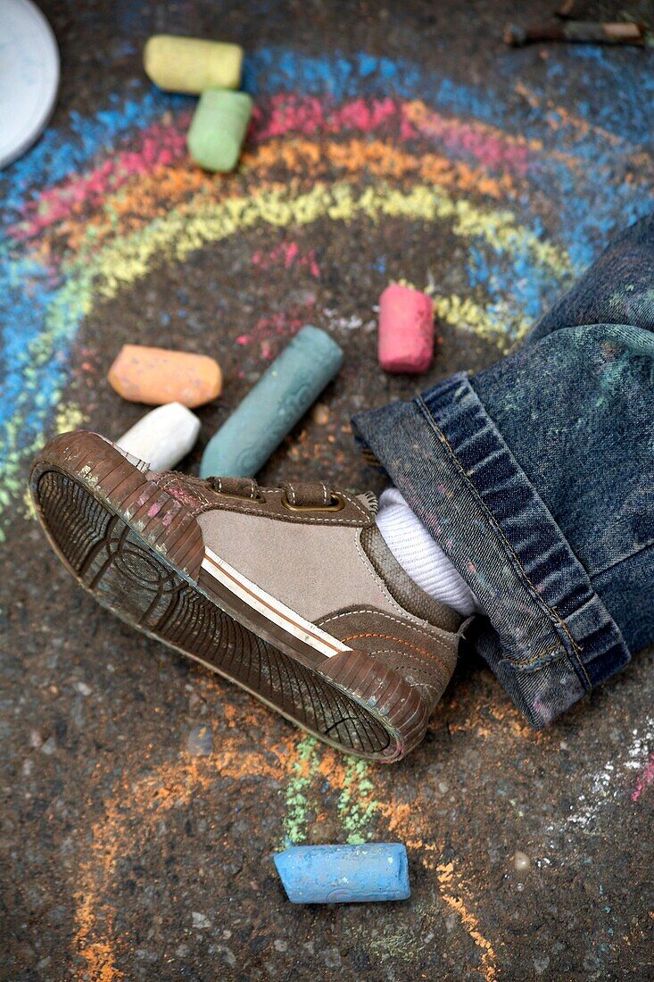 An overhead photograph of a 2 year old boy's shoe on a sidewalk surrounded by chalk and drawings
