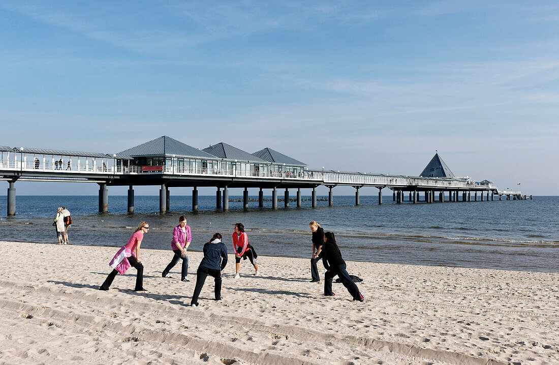 Women stretchig at beach, pier in background, Heringsdorf, Usedom, Mecklenburg-Vorpommern, Germany