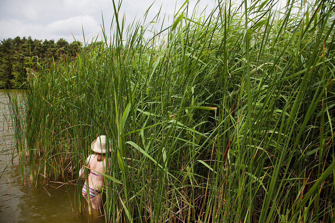 Girl wearing straw hat standing between reeds in lake Teupitz, Brandenburg, Germany