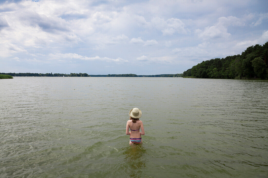 Girl wearing straw hat standing in lake Teupitz, Brandenburg, Germany