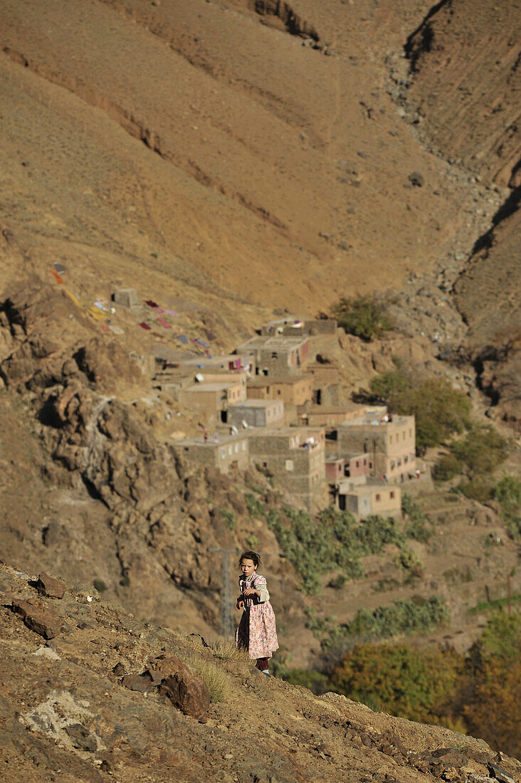 Girl in the mountains, houses of a village in the back, Marrekech area,  High Atlas, Morocco