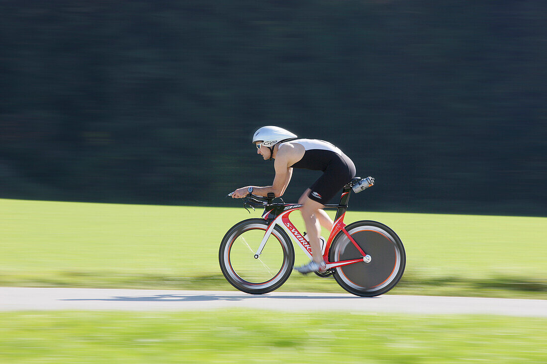 Male racing cyclist with disc wheel on road near Munsing, Upper Bavaria, Germany