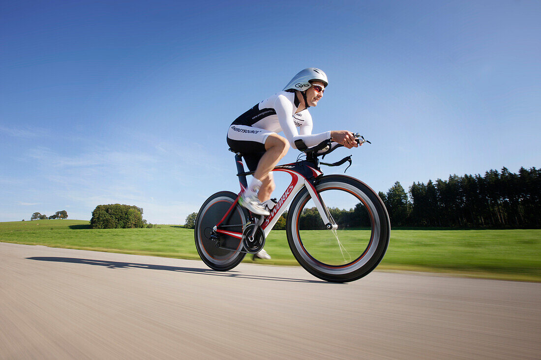 Male racing cyclist with disc wheel on road near Munsing, Upper Bavaria, Germany