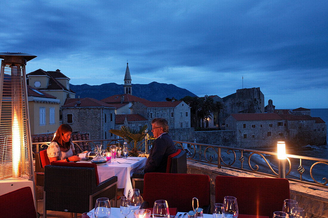 Couple on the terrace of the Astoria restaurant in the evening, view of citadel, Budva, Montenegro, Europe