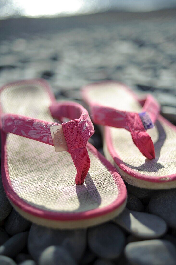 A pair of pink flip flops shoes on a pebble beach, summer UK