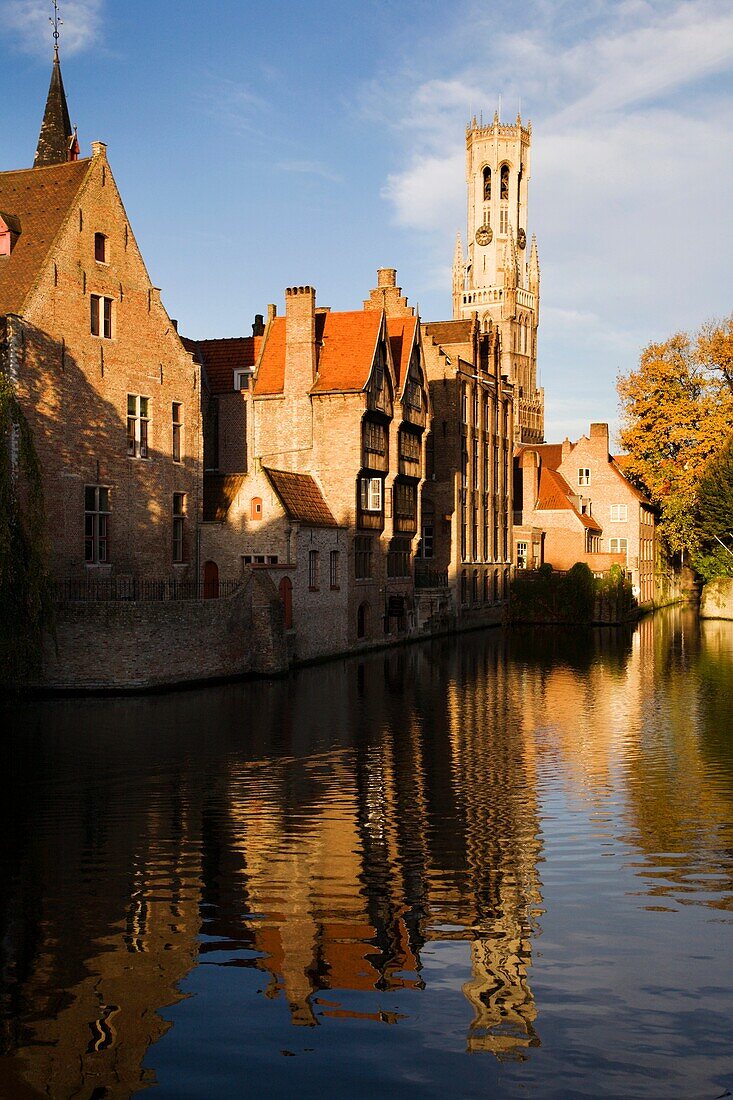 The Belfort reflected in the River Dijver in morning sunshine Bruges Belgium