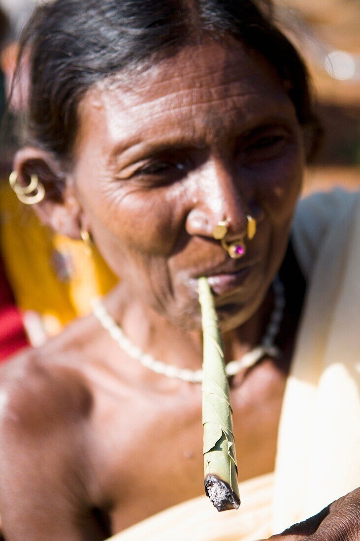 A tribal woman from Orissa smoking a traditional rolled cigarette.