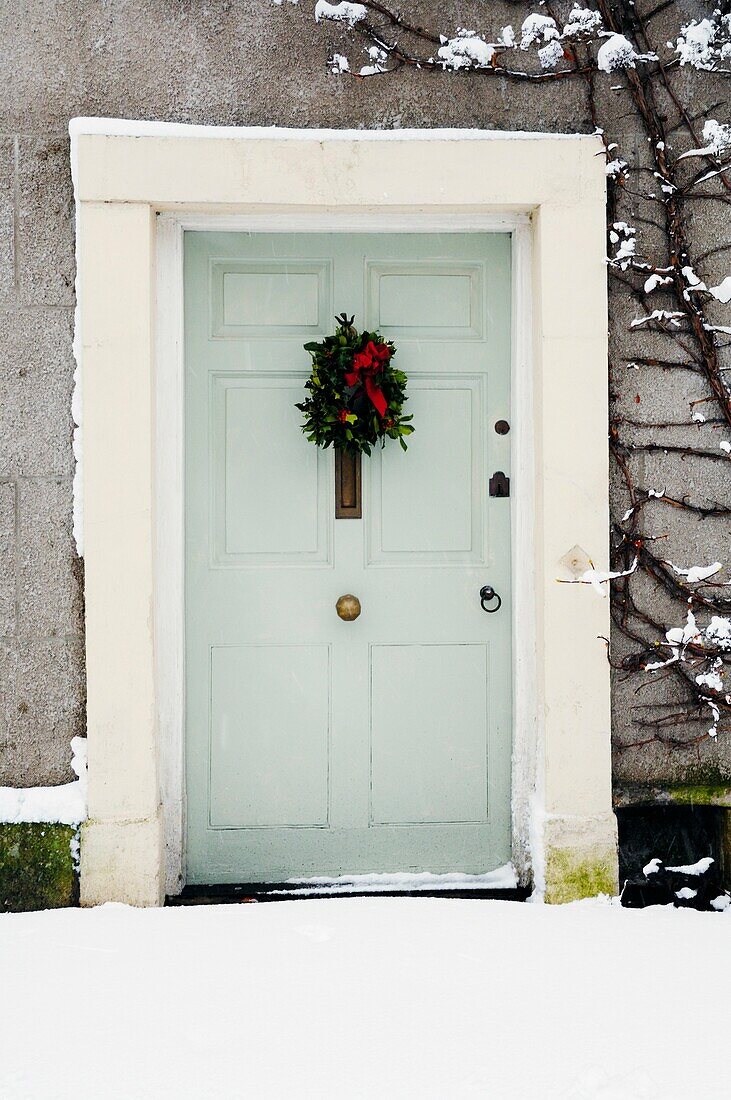 A front door and christmas decoration surrounded by fresh snowfall