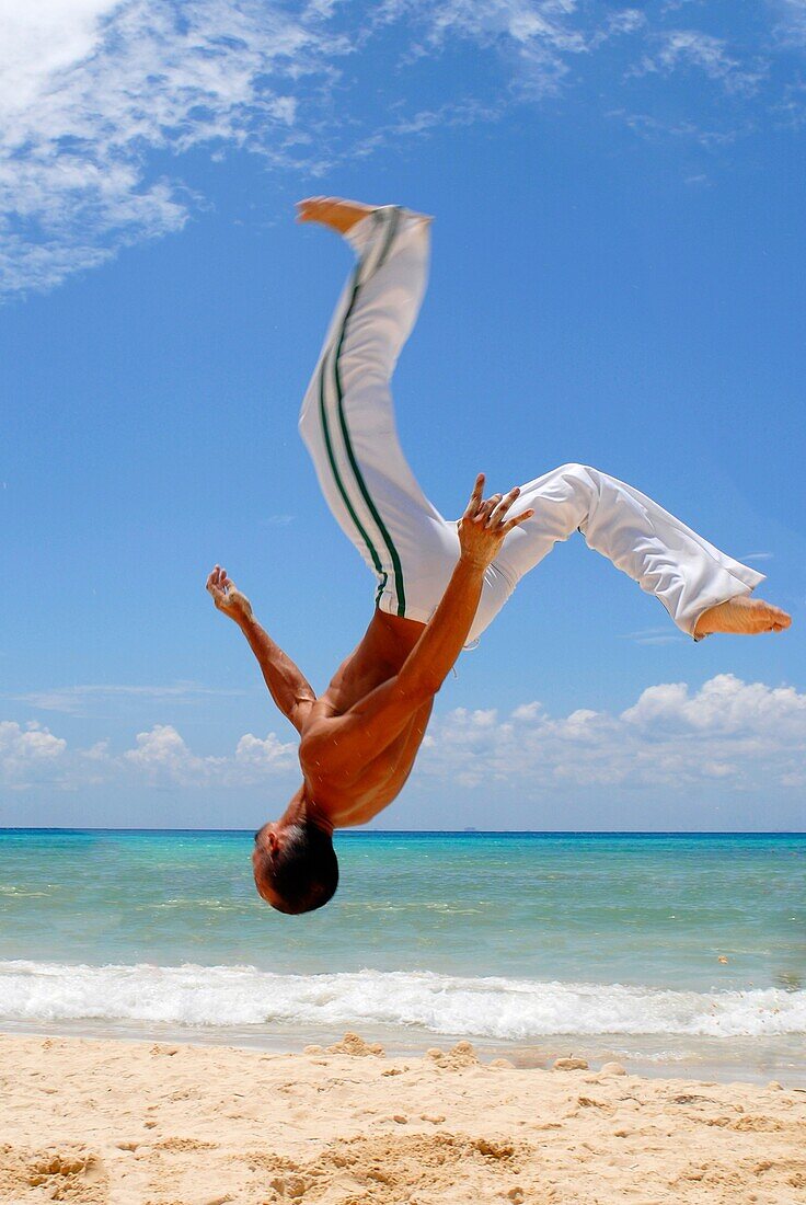 A man practicing Capoeira on the beach