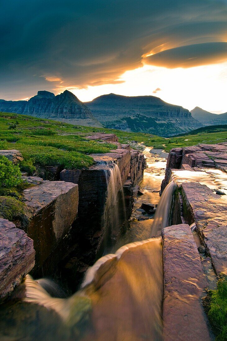 Lenticular cloud at dawn over the triple waterfalls at Logan Pass in Glacier National Park