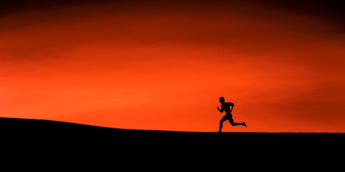 The silhouette of a man running up a slight incline, high contrast of land, figure and crimson sky