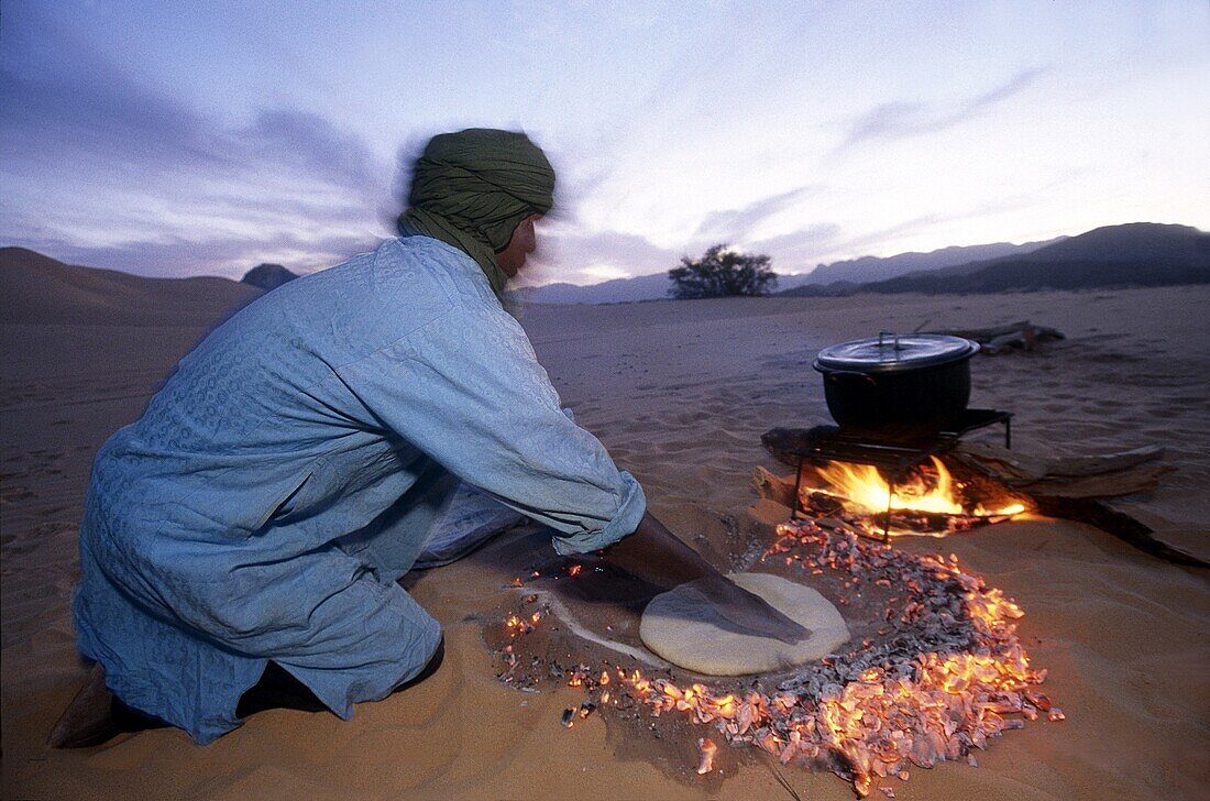 Mann backt Brotteig im von der Glut erhitzten Sand, Wüste Aïr, Niger, Westafrika