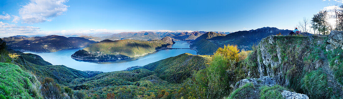 Panorama mit Frau auf Aussichtsbank, Blick auf Luganer See mit Tessiner Alpen, Luganer See, Blick vom Monte San Giorgio, UNESCO Welterbe Monte San Giorgio, Tessin, Schweiz, Europa