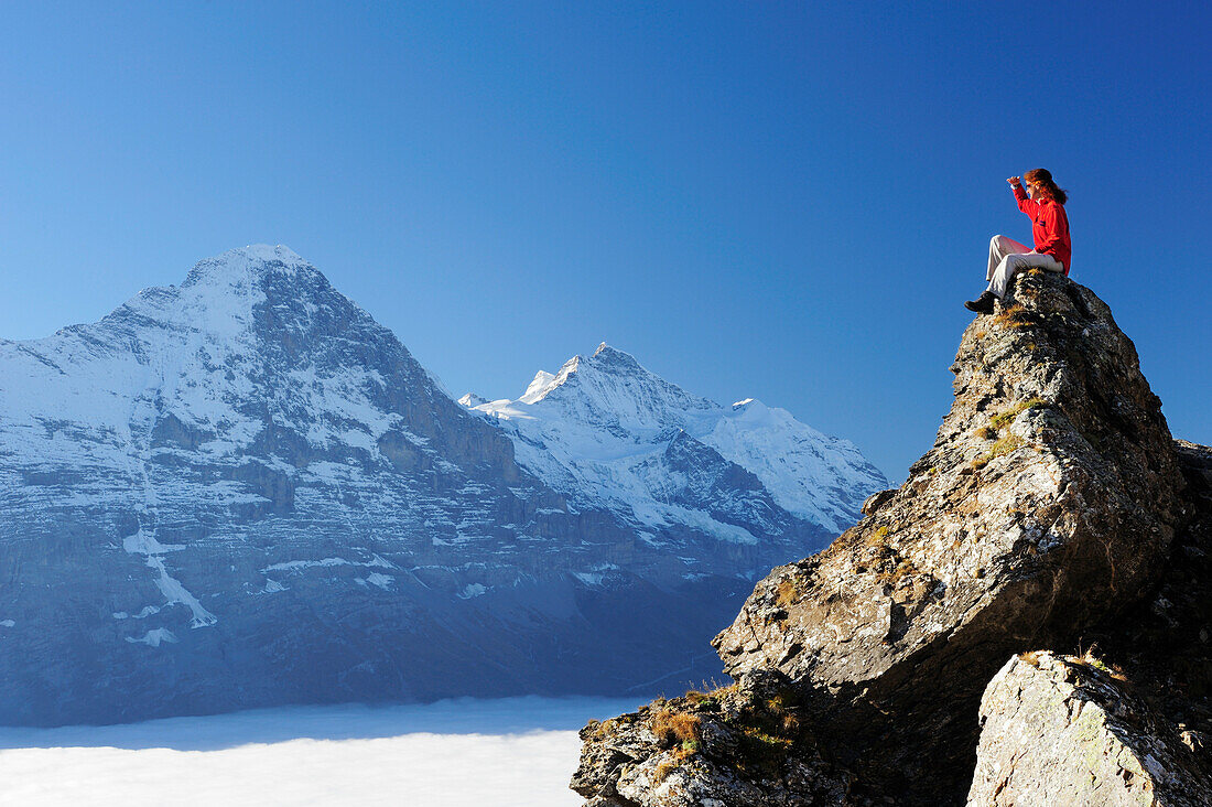 Frau sitzt auf Felsen und blickt auf Eiger und Jungfrau über Nebelmeer, Bussalp, Grindelwald, UNESCO Welterbe Schweizer Alpen Jungfrau - Aletsch, Berner Oberland, Bern, Schweiz, Europa
