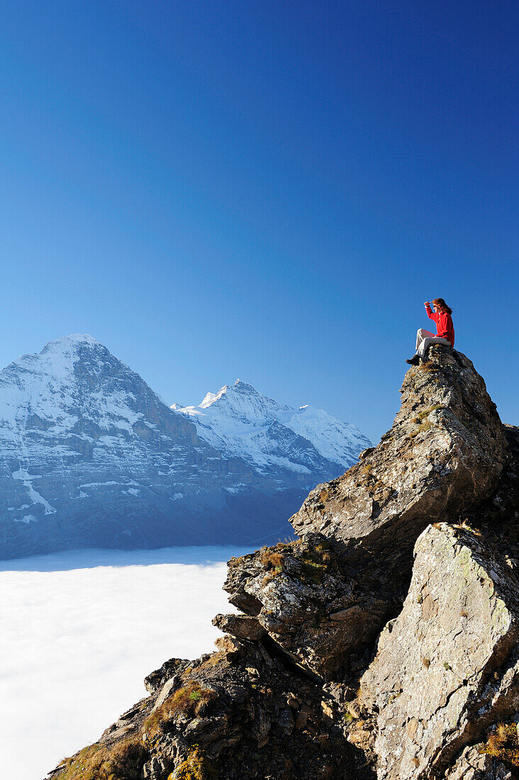 Frau sitzt auf Felsen und blickt auf Eiger und Jungfrau über Nebelmeer, Bussalp, Grindelwald, UNESCO Welterbe Schweizer Alpen Jungfrau - Aletsch, Berner Oberland, Bern, Schweiz, Europa