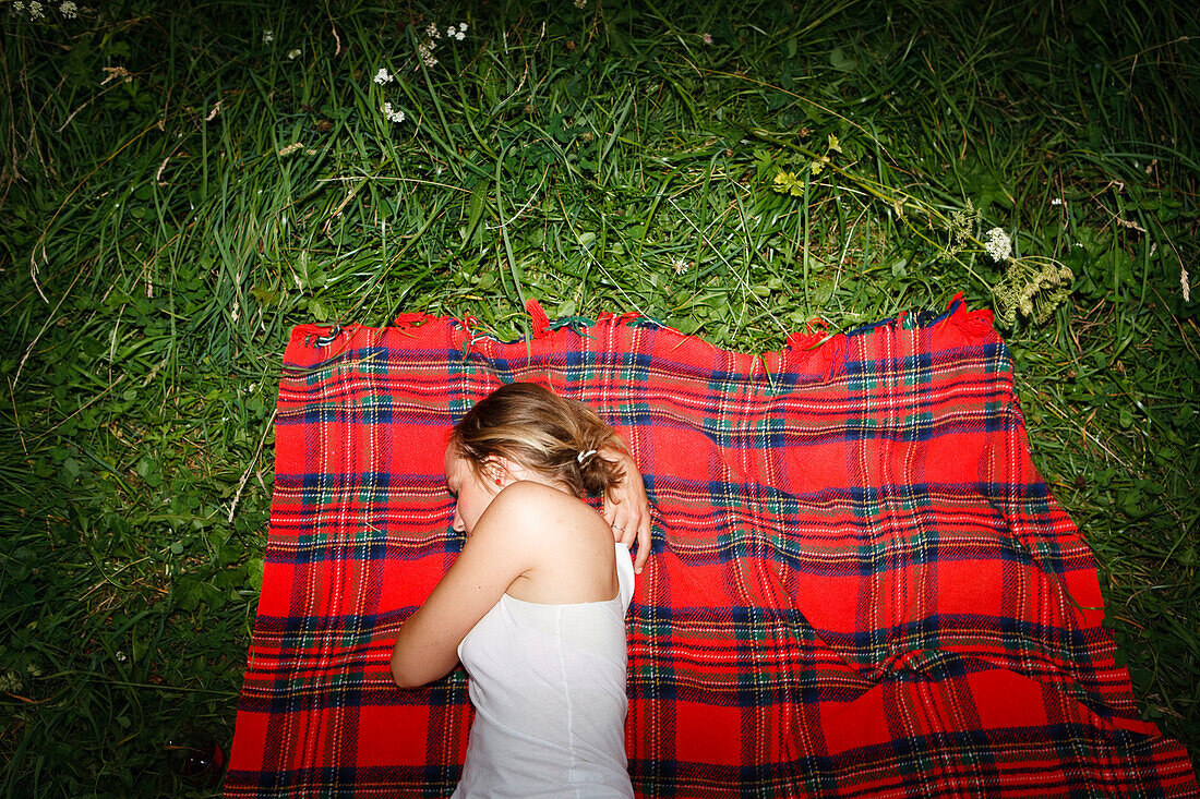 Young woman lying on red checked blanket on grass