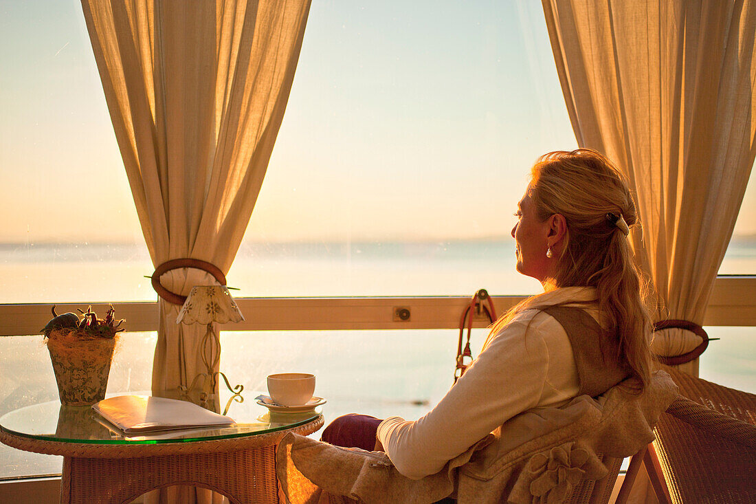 Eine Frau in Café mit Blick auf den Chiemsee, Chieming, Chiemsee, Chiemgau, Oberbayern, Bayern, Deutschland