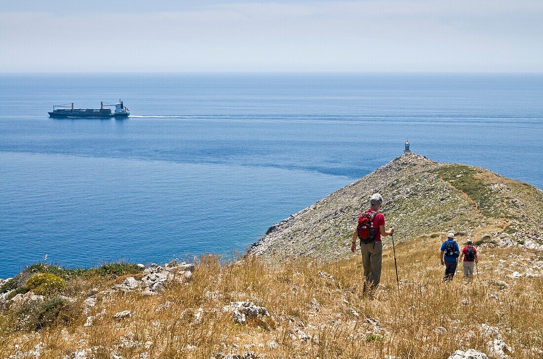 Walkers on a ridge descending to the Lighthouse at the tip of Cape Tenaro in the deep Mani, Peloponnese, Greece