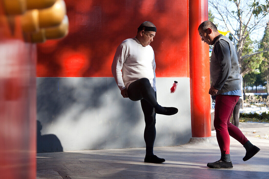 Morgensport im Jingshan Park, zwei alte Männer spielen Federball mit den Füßen, rote Mauer, Westtor,  Körperertüchtigung, Peking, China