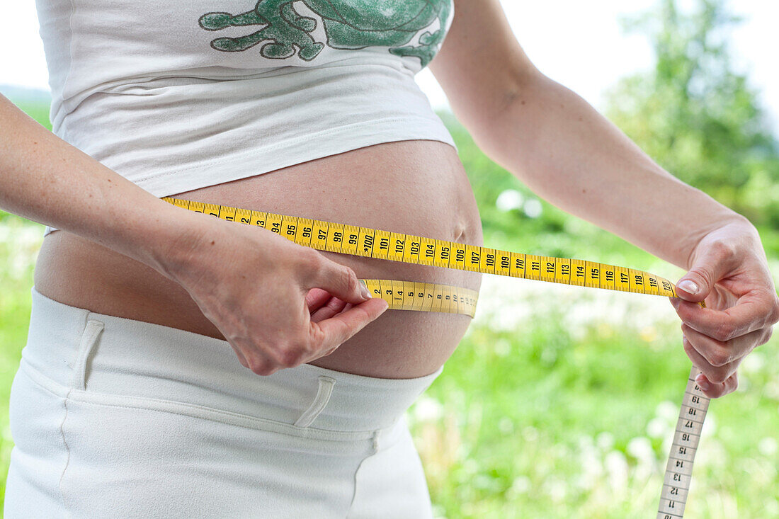 Pregnant woman measuring her belly with measuring tape, Rerik, Mecklenburg-Western Pomerania, Germany