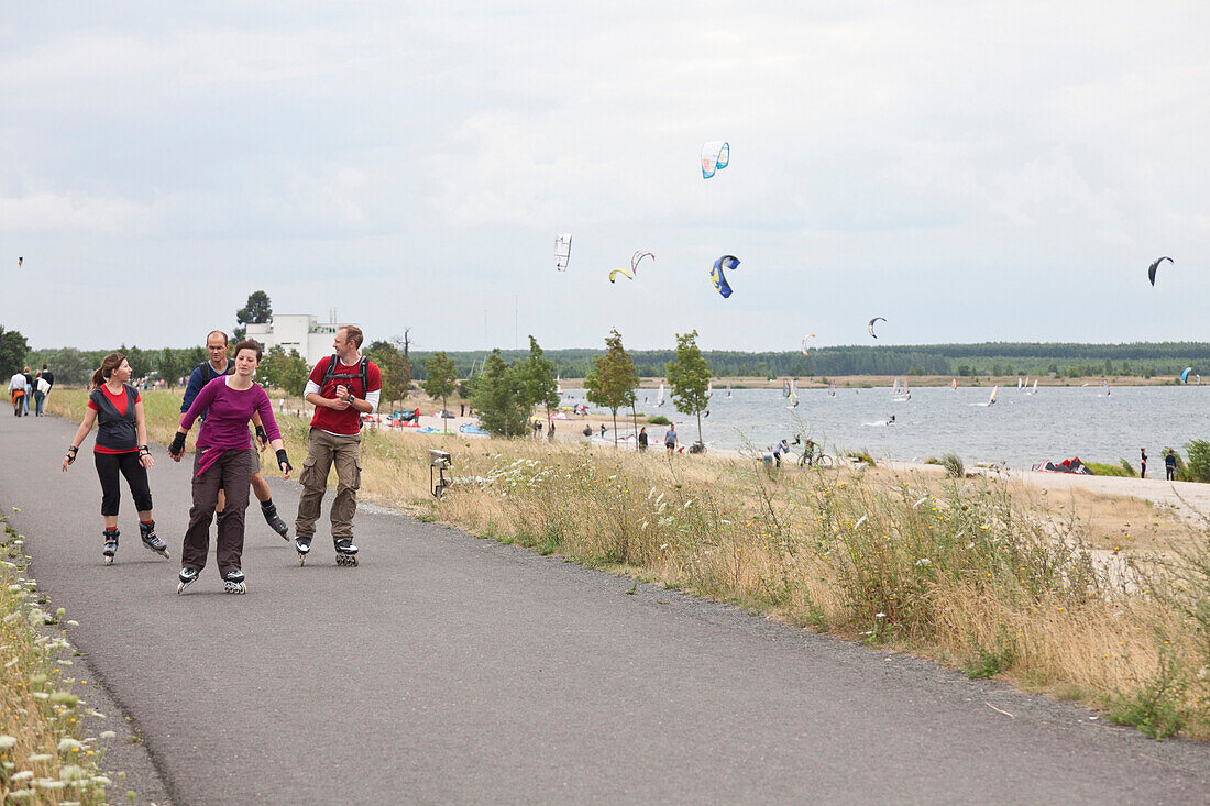 In-line skaters, kite surfers at Cospuden Lake in background, Leipzig, Saxony, Germany